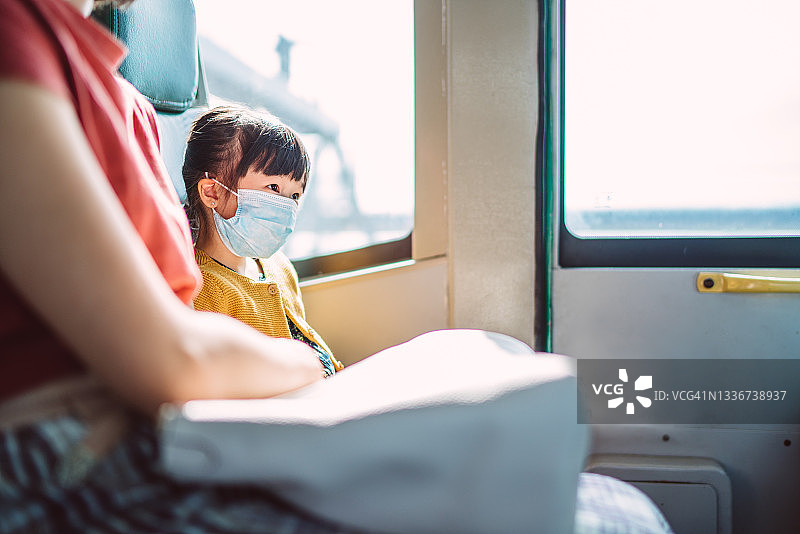 戴着防护口罩的小女孩高兴地和妈妈一起乘公共汽车图片素材