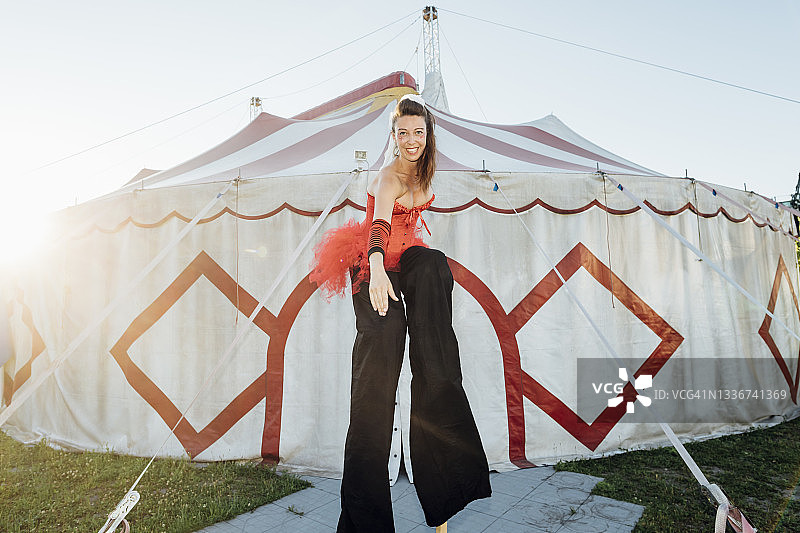 笑容满面的女子在马戏团帐篷前踩高跷伸展身体图片素材