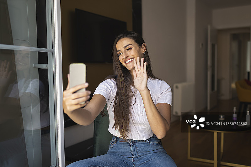 微笑的年轻女子在使用智能手机进行视频通话时挥手图片素材