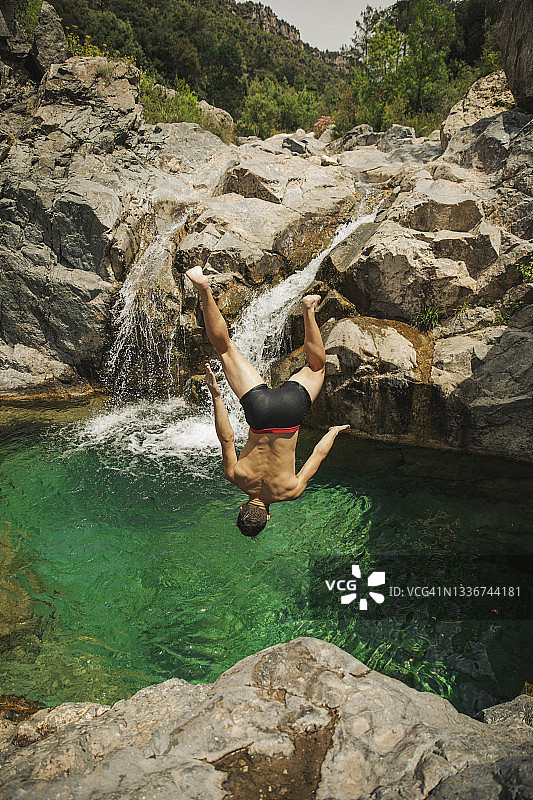 阳光明媚的日子里，赤膊男人在瀑布中跳跃图片素材