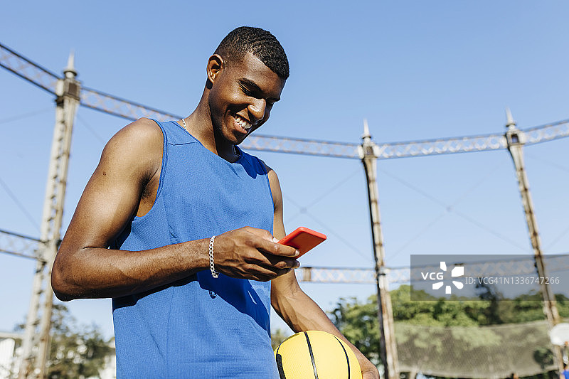 在篮球场使用智能手机的微笑年轻人图片素材