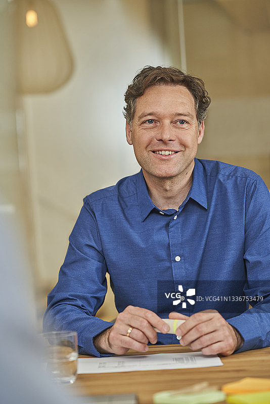 微笑的商人坐在会议桌旁看向远方图片素材