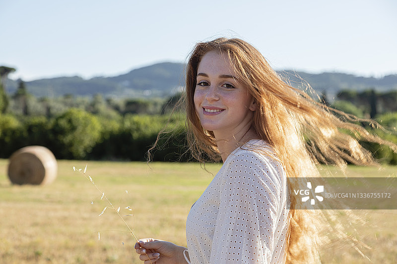年轻红发女子在田野上微笑图片素材