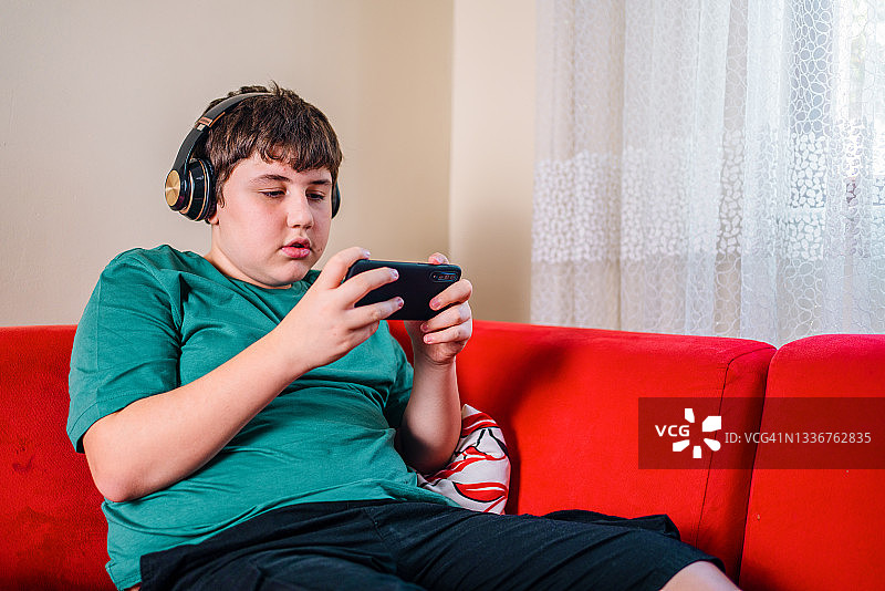 男孩在客厅戴着耳机用智能手机玩多人在线游戏图片素材
