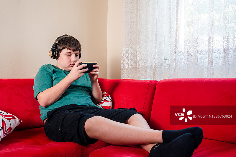 男孩在客厅戴着耳机用智能手机玩多人在线游戏图片素材