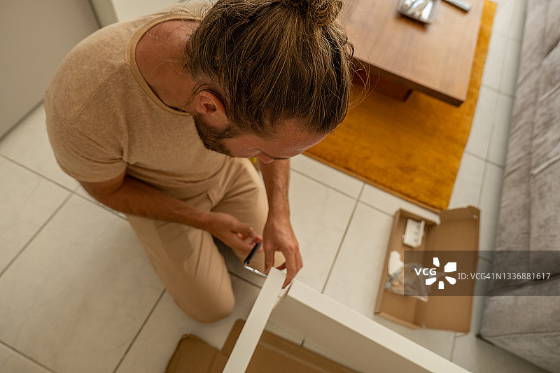 年轻男人在新家组装扁平包装家具图片素材