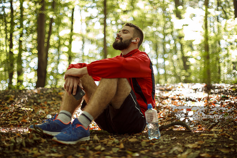 戴蓝牙耳机在森林中休息的年轻男子图片素材