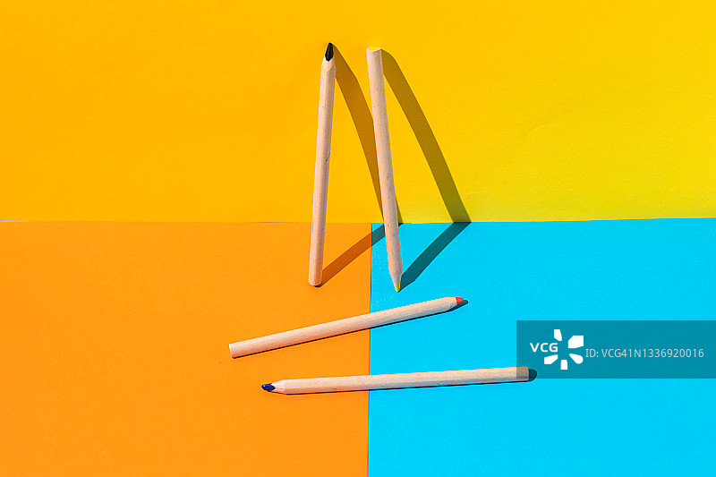 靠在黄色墙壁上的两支木制铅笔和放在蓝橙色地板上的两支木制铅笔：学校、办公室和文具概念图片素材