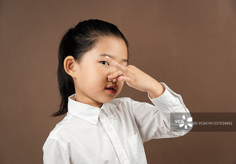 在棕色背景上捏鼻子的小女孩图片素材