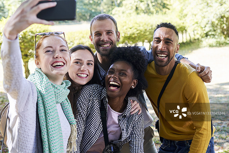 笑容满面的女人在公园与朋友们站在一起，用智能手机自拍图片素材