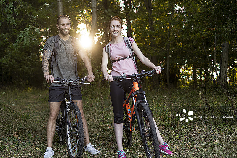 在森林里，一对年轻情侣推着自行车微笑图片素材