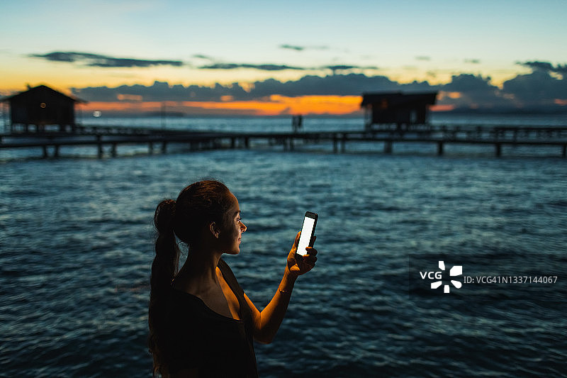 女人在热带岛屿日落时享受生活，与家人朋友视频聊天图片素材