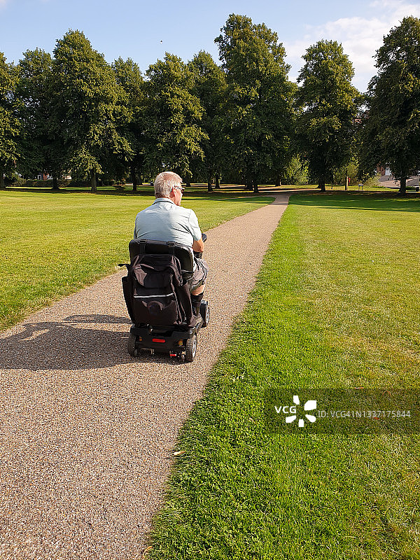 一位男子在什鲁斯伯里什罗普郡的公园里骑着他的电动代步车，享受着车辆给予他的自由和独立，因为他无法行走图片素材