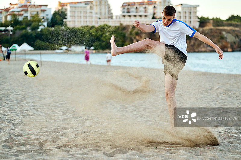 在沙滩上踢球的青少年男孩图片素材