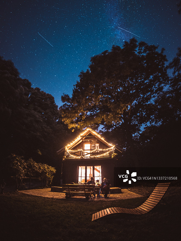 温馨的生态森林小屋，在英仙座流星雨期间位于银河之下图片素材