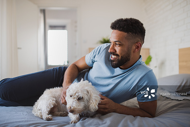 年轻男人和狗在室内床上休息的肖像照图片素材