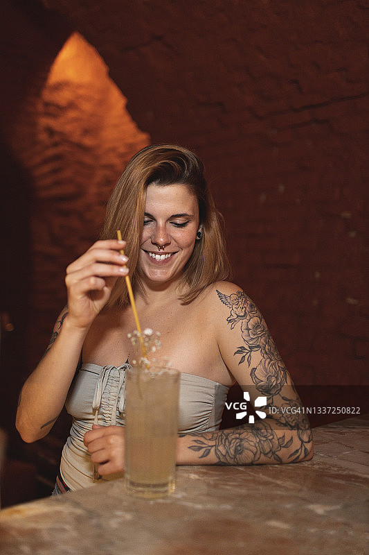 在酒吧柜台拿着鸡尾酒的微笑纹身女人图片素材