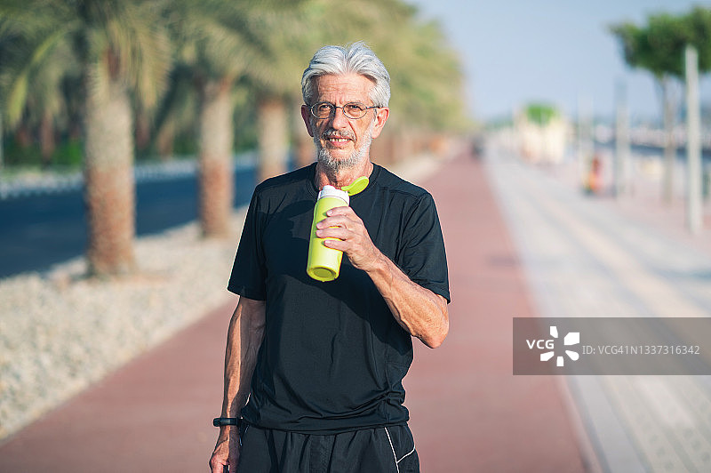 在跑道上慢跑后喝水补充水分的年长男人图片素材