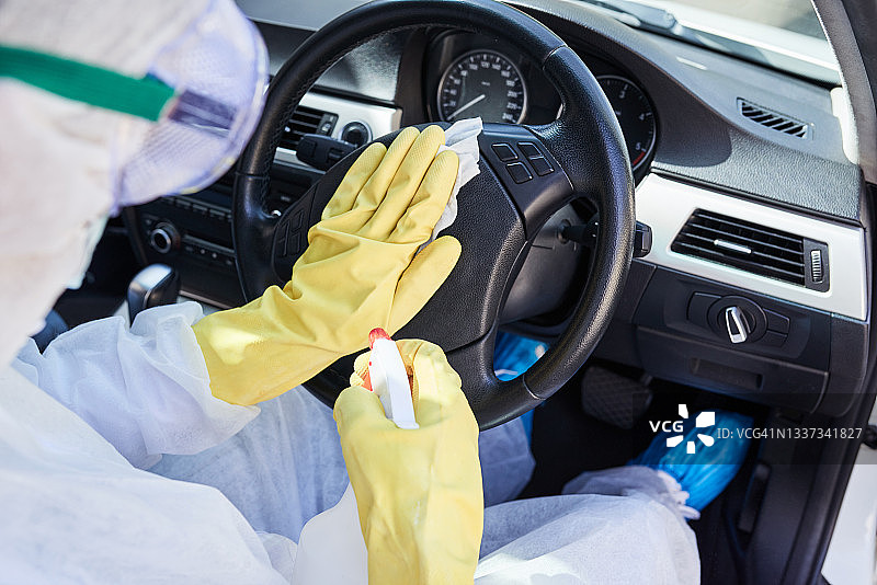 一位身份不明的清洁人员在汽车中消毒方向盘的特写镜头图片素材