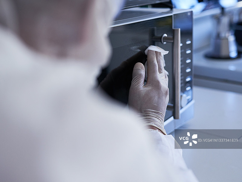 厨房里一位身份不明的清洁工擦拭微波炉的特写镜头图片素材