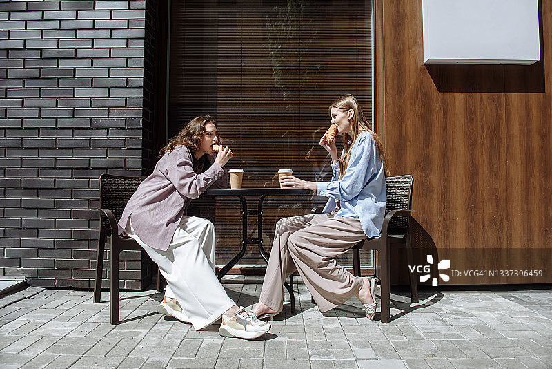两个年轻女人坐在咖啡馆里边吃边聊图片素材