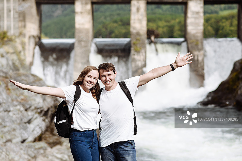 在阿尔泰水电站瀑布背景下的幸福游客情侣图片素材