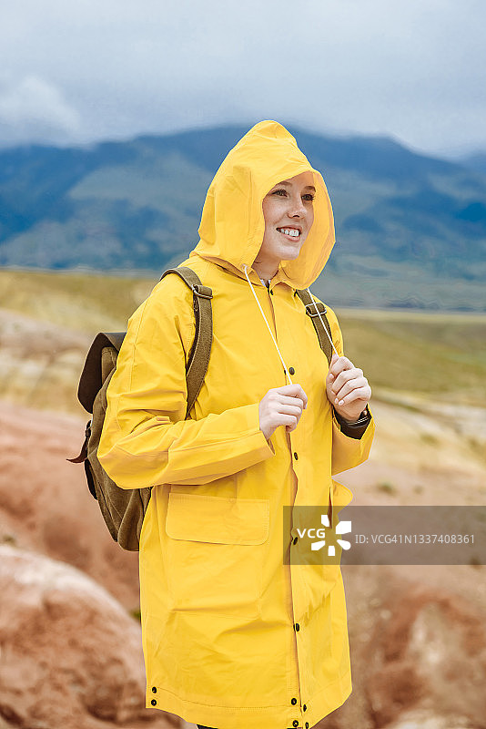 快乐的女游客身穿黄色夹克，站在彩色山顶上，带着背包。在阿尔泰的火星原野上微笑的女人。旅行和度假概念图片素材