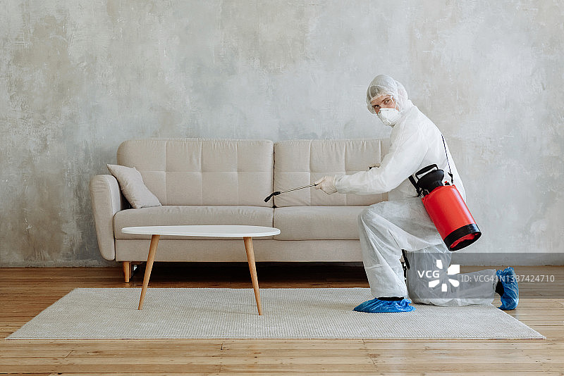 穿防护服的男消毒员在房子里喷洒消毒剂，预防措施，复制空间。化学物质去除冠状病毒和COVID-19图片素材