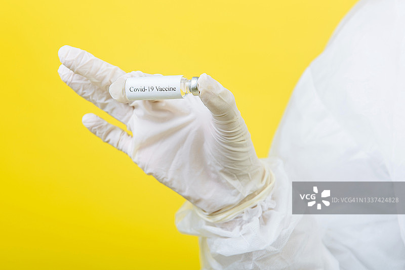 医生穿着防护服（PPE）手持新冠疫苗的特写.Covid-19图片素材