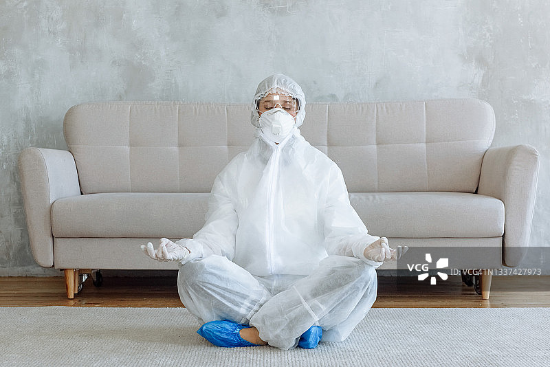 穿防护服的消毒人员在家中沙发前呈莲花座姿势，新冠病毒疫情消毒概念，家庭消毒图片素材