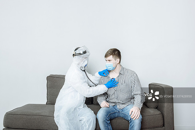 医生身穿防护服，戴着口罩和手套，用听诊器检查新冠肺炎患者的呼吸图片素材