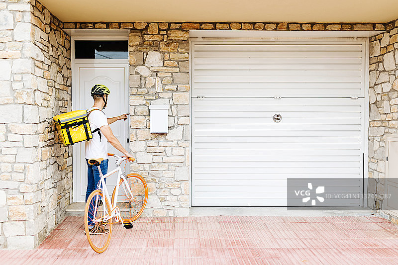 西班牙裔男性快递员骑自行车按门铃送餐图片素材