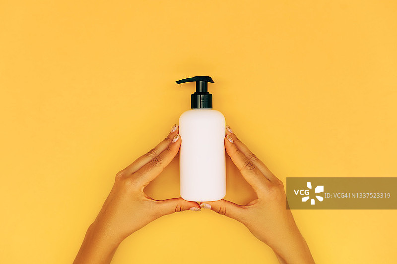 女人手持带分配器的白色塑料瓶，黄色背景图片素材