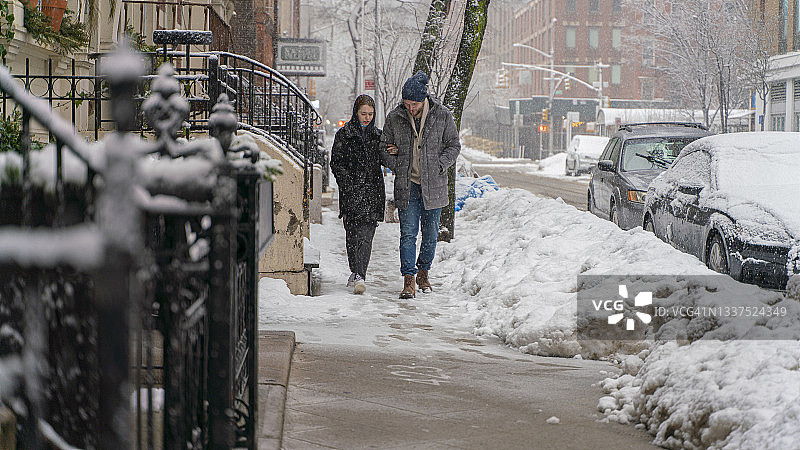 在因冬季降雪而空无一人的城市街道上沿着人行道行走的年轻朋友图片素材