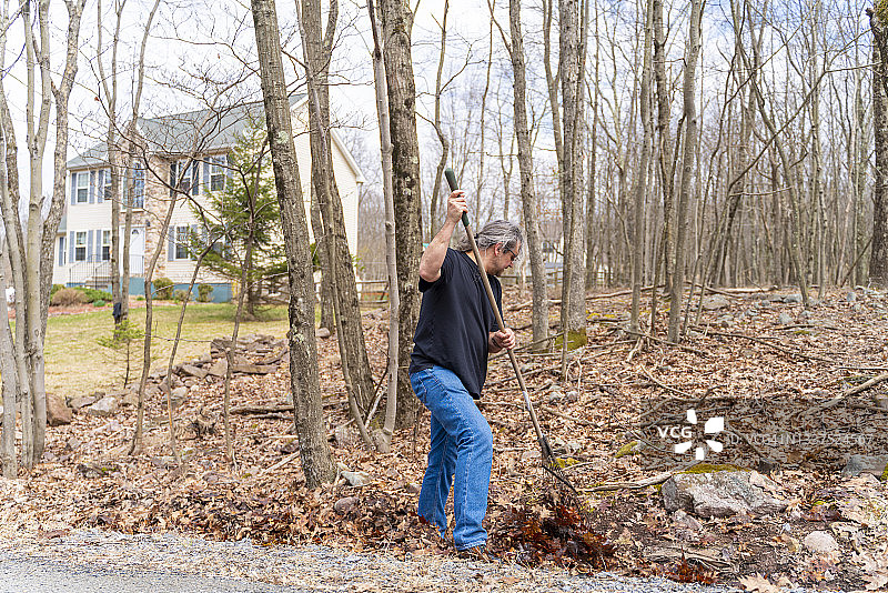 扎着马尾辫的50岁男子正在清理后院的落叶图片素材