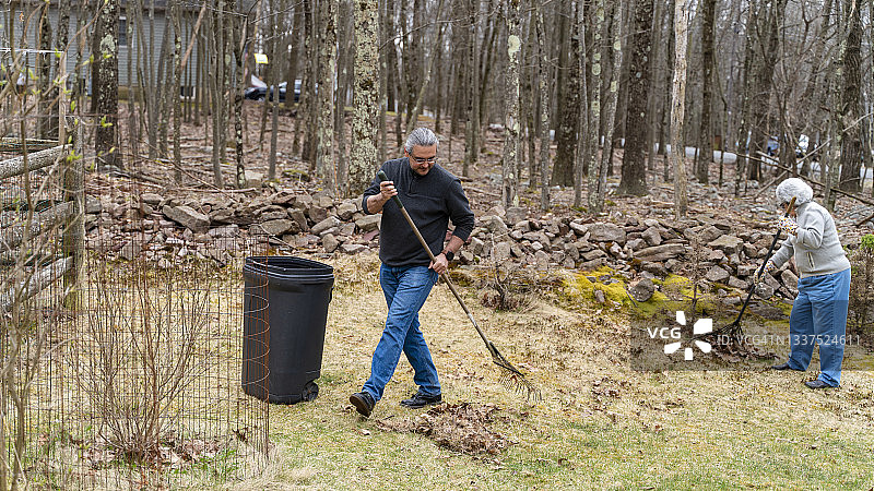 中年男人帮助年长的母亲清理乡间小屋后院的落叶图片素材