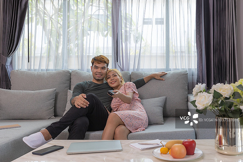 亚洲夫妇坐在沙发上，使用电视遥控器图片素材