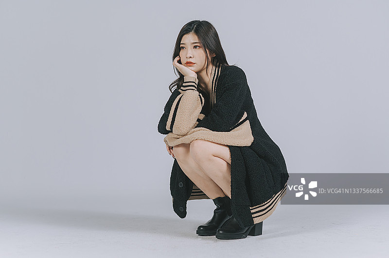 亚洲中国美女蹲伏手托下巴灰色背景工作室拍摄图片素材