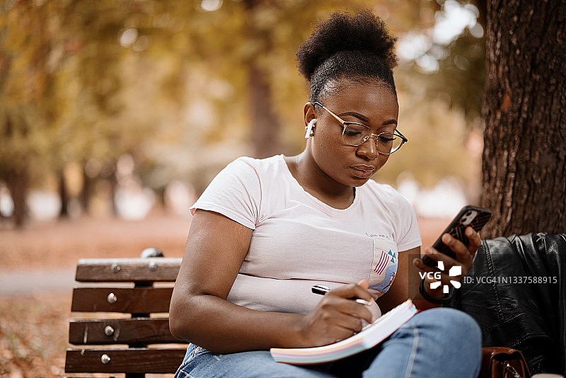 专注的千禧一代黑人女性在笔记本上写东西图片素材