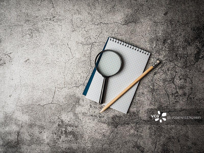 水泥背景上的笔记本、铅笔和放大镜——研究调查概念图片素材