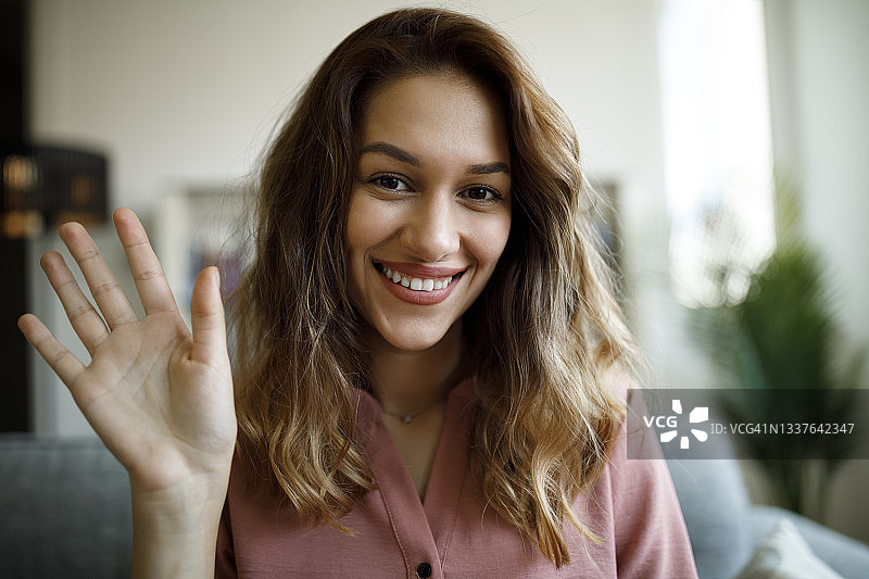 年轻微笑的女人在家居办公室的视频通话中挥手图片素材