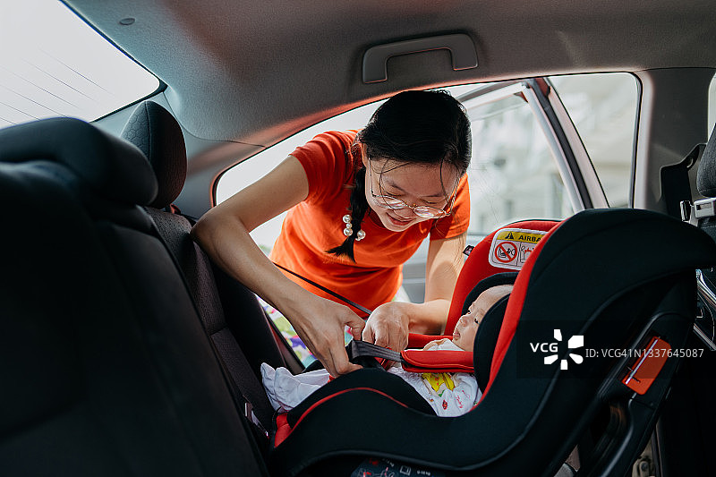 母亲为汽车安全座椅上的宝宝系安全带图片素材