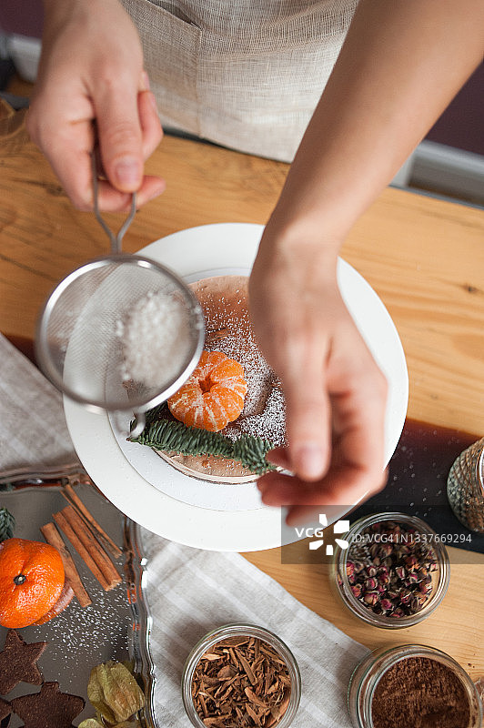 糕点师用云杉枝、橘子、巧克力饼干星星和椰子片装饰纯素巧克力蛋糕，用于圣诞晚餐图片素材