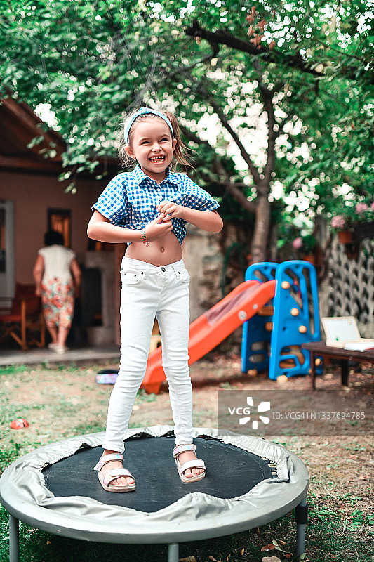 可爱女童在自家后院蹦床上跳跃图片素材