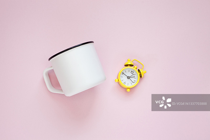粉色背景上的白色杯子和黄色复古闹钟，早晨概念图片素材