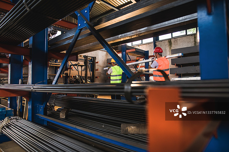 工厂里合作搬运钢材的两名金属工人图片素材