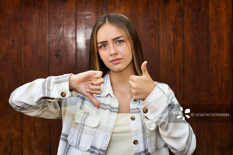 困惑地看着镜头并竖起大拇指和倒拇指的年轻拉丁裔女人图片素材