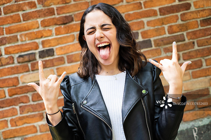 一位拉丁裔女子看着镜头，做着重金属摇滚手势图片素材