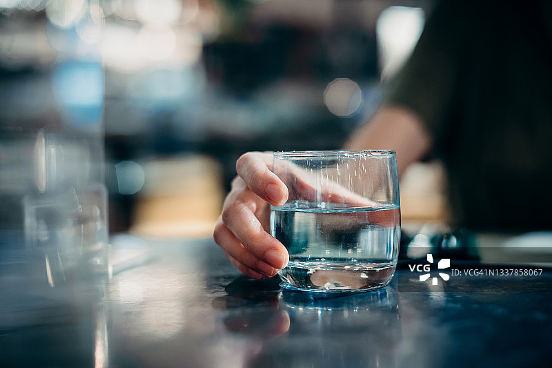 年轻女人在餐厅餐桌旁喝水的特写：健康生活，保持水分充足图片素材