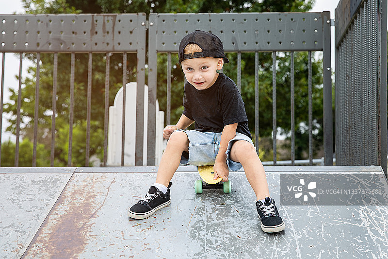 男孩在滑板公园的斜坡上玩滑板，面带微笑图片素材